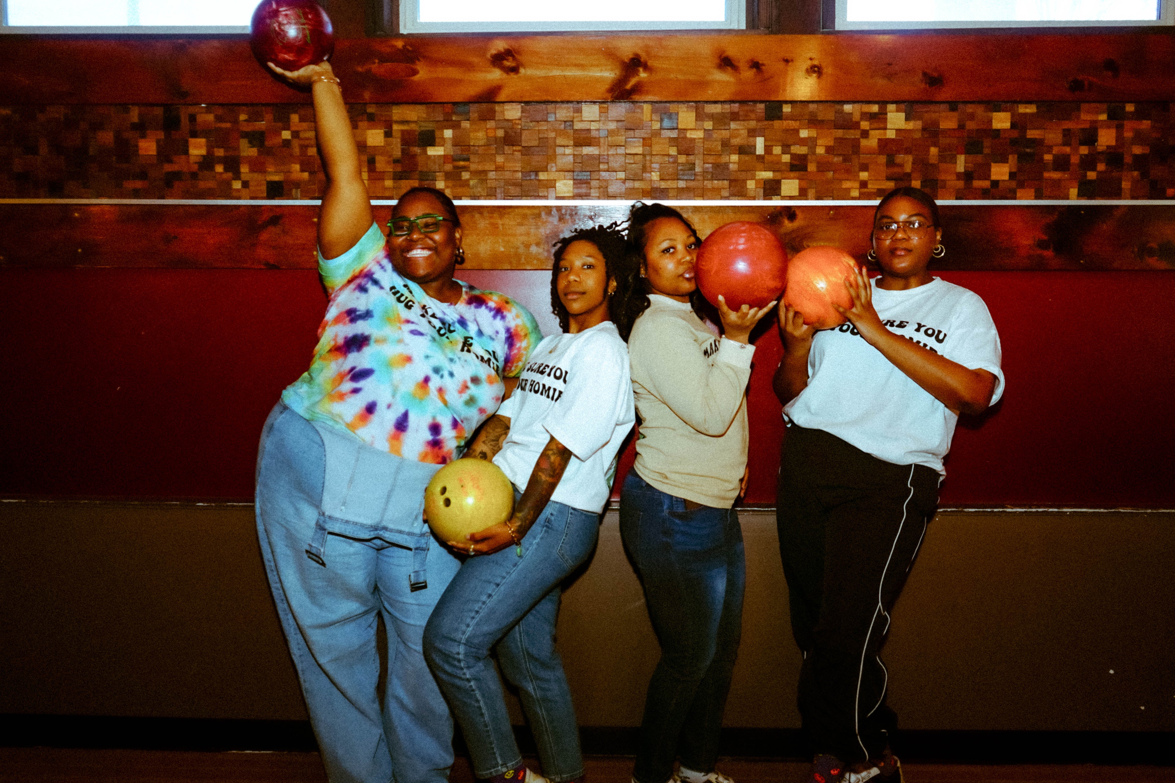 A group women of color posing with bowling balls in a bowling alley