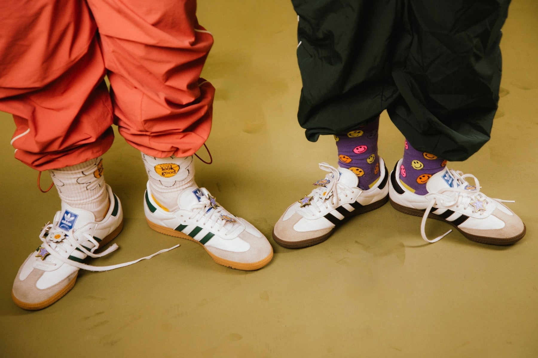 two women wearing adidas with not a bad life enamel pins on laces