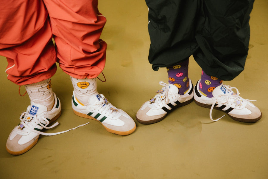 two women wearing adidas with not a bad life enamel pins on laces